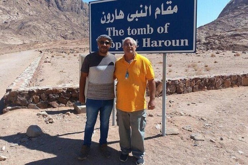 Two men standing in front of a sign that reads 'The tomb of Prophet Haroun' in both Arabic and English. 4