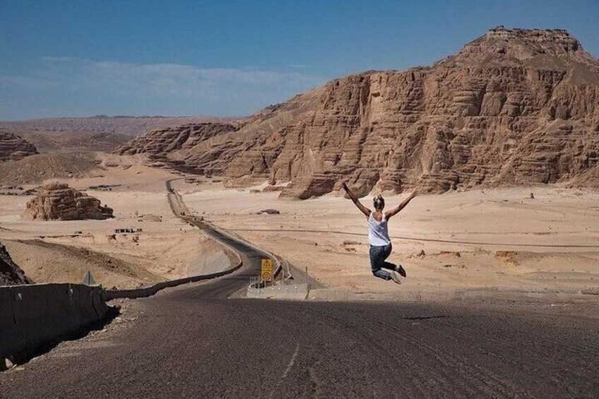 A person jumping in a desert with a winding road and rocky hills in the background. 4