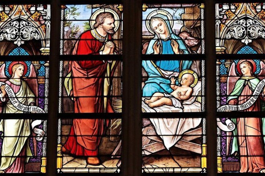 A stained glass window with religious figures, including a central figure in red and a child in blue, surrounded by angels. 3