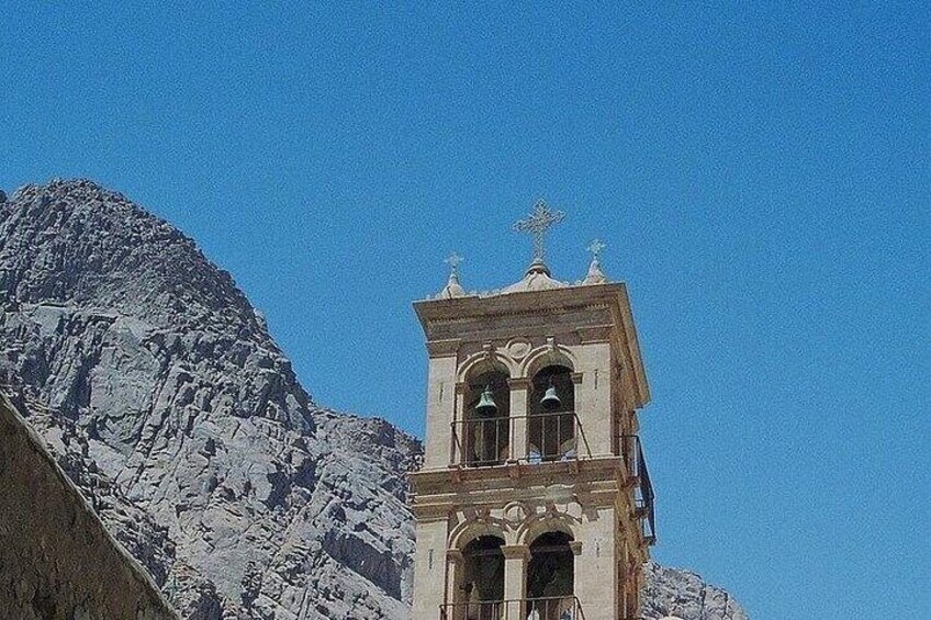 A bell tower with a cross on top, set against a mountainous backdrop. 5