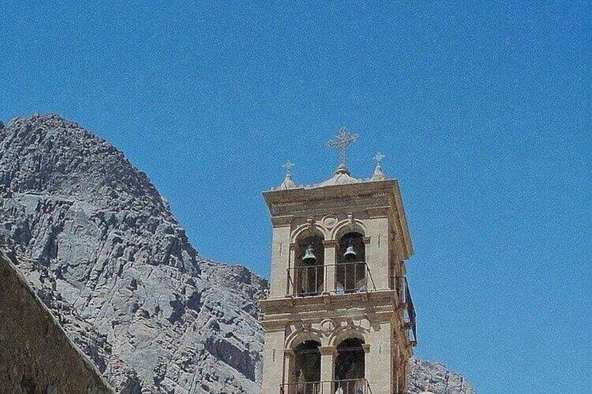 A bell tower with arched windows and a cross on top, set against a mountainous backdrop. 5