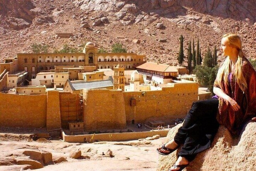 A person sitting on a sandy hill overlooking a model of a historical city with buildings and a fortress. 3
