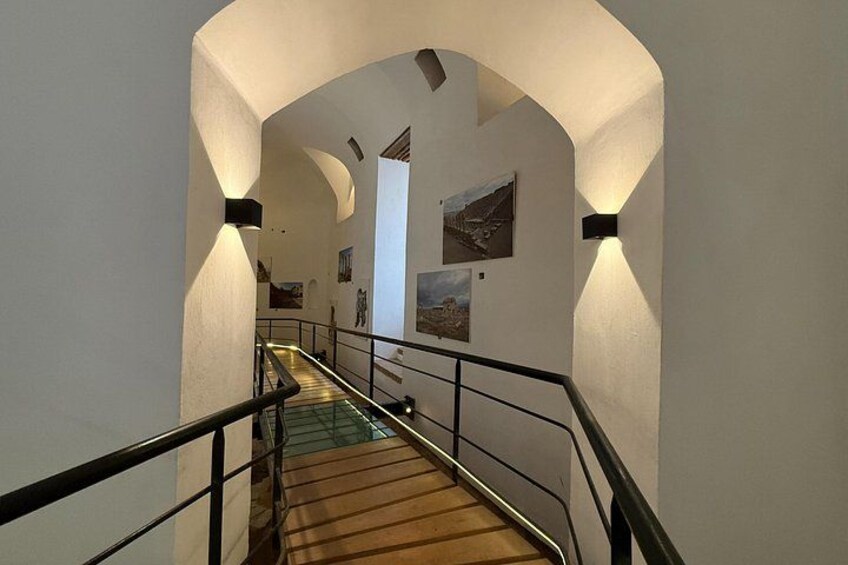 Una escalera con barandilla de vidrio, paredes blancas y cuadros enmarcados. 2