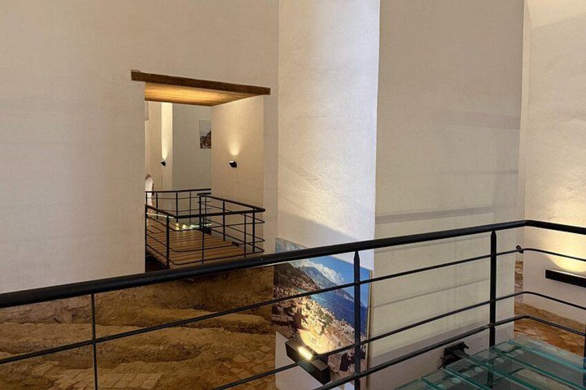 Un interior moderno con barandilla de vidrio, suelo de piedra y vistas a un paisaje montañoso. 3