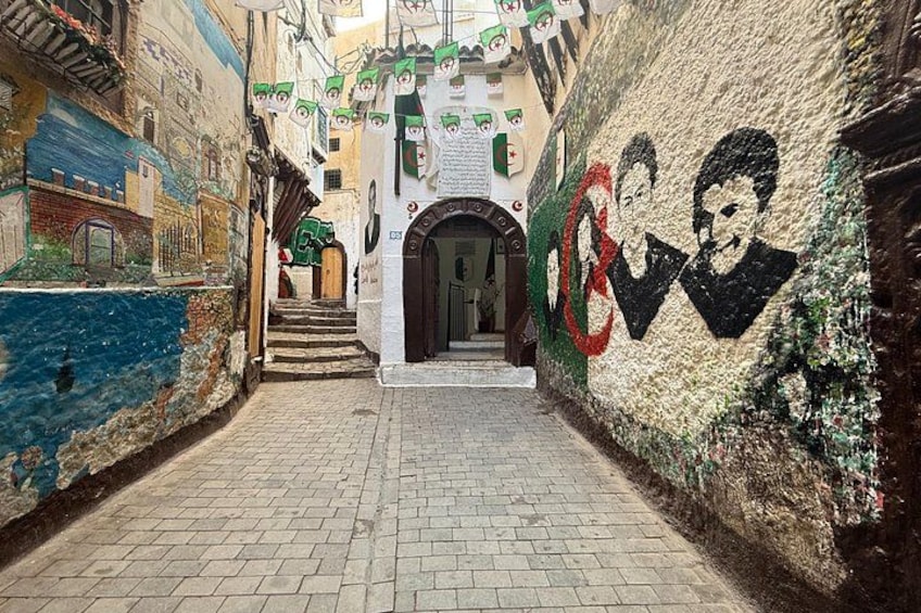 Un callejón estrecho con un mural, una escalera y una puerta. 5