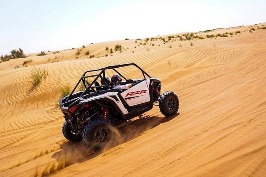 A white off-road vehicle with 'RZR' on the side driving through a sandy desert landscape. 3