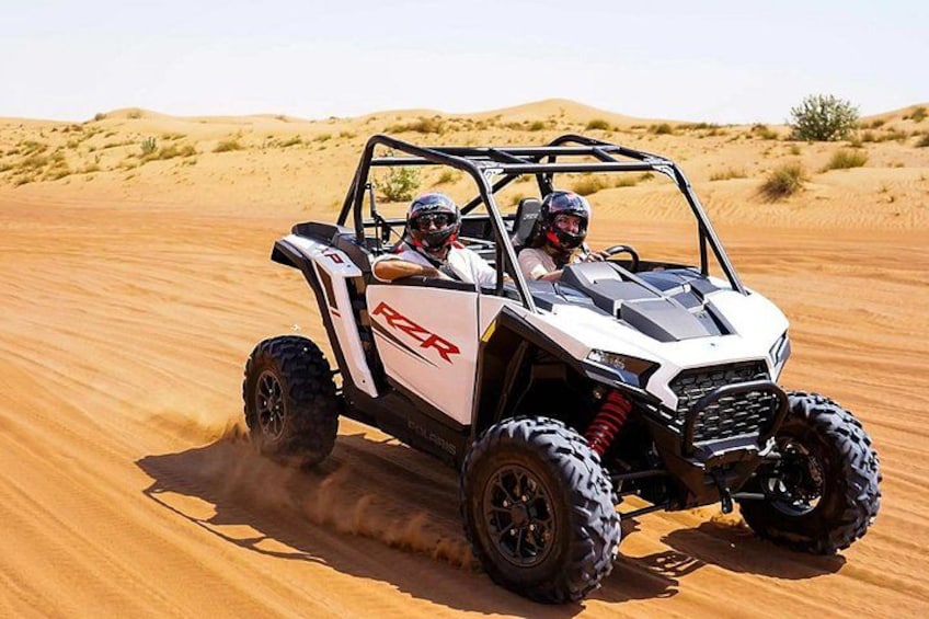 A white off-road vehicle with large tires driving on a sandy terrain. 2