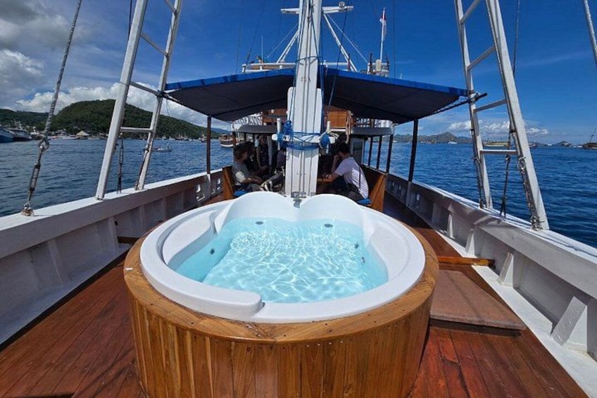 Un bateau avec un pont en bois, un jacuzzi et une personne assise au poste de pilotage. 2