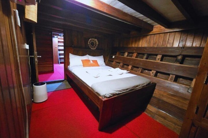 A wooden cabin interior with a bed, red carpet, and a circular wall decoration. 3