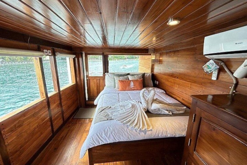 A wooden cabin interior with a bed, windows, and a wall-mounted air conditioner. 3