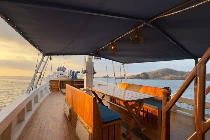 A wooden deck with a table and benches, a covered area, and a view of the sea and hills in the background. 4