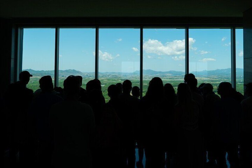 Un grupo de personas dentro de un edificio observando un paisaje con montañas y cielo despejado. 3