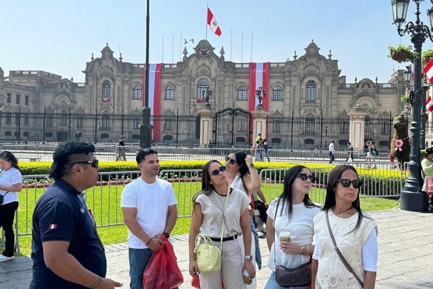 A group of people standing in front of a large, ornate building with flags. 1