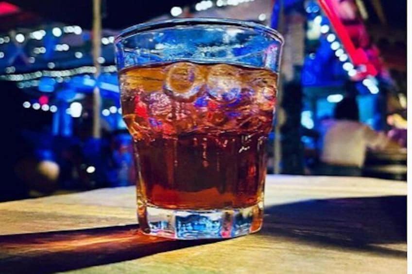 A glass of amber-colored beverage with ice cubes on a wooden surface. 3