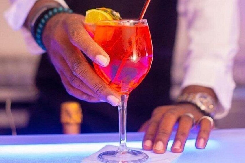 A hand holding a cocktail glass with a red drink, garnished with a slice of lemon and a straw. 2