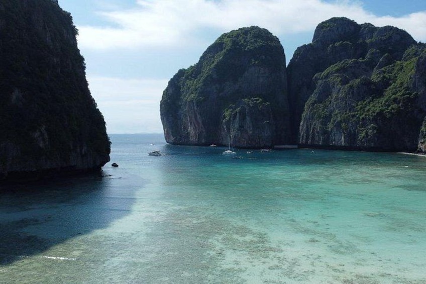 A coastal landscape with clear turquoise waters, large rock formations, and a small boat in the distance. 2