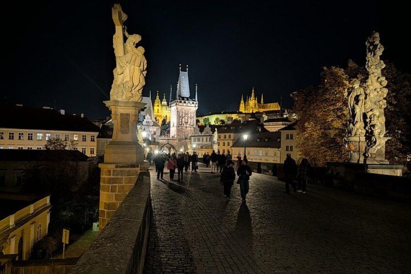 A nighttime view of a historic square with statues, cobblestone pavement, and illuminated buildings in the background. 3