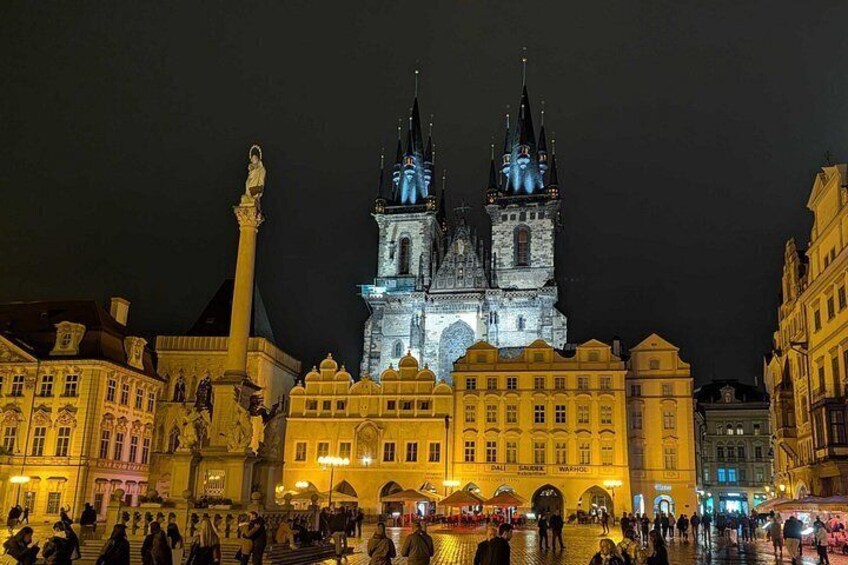 A historic building with two towers, a statue, and a crowd in a square. 5