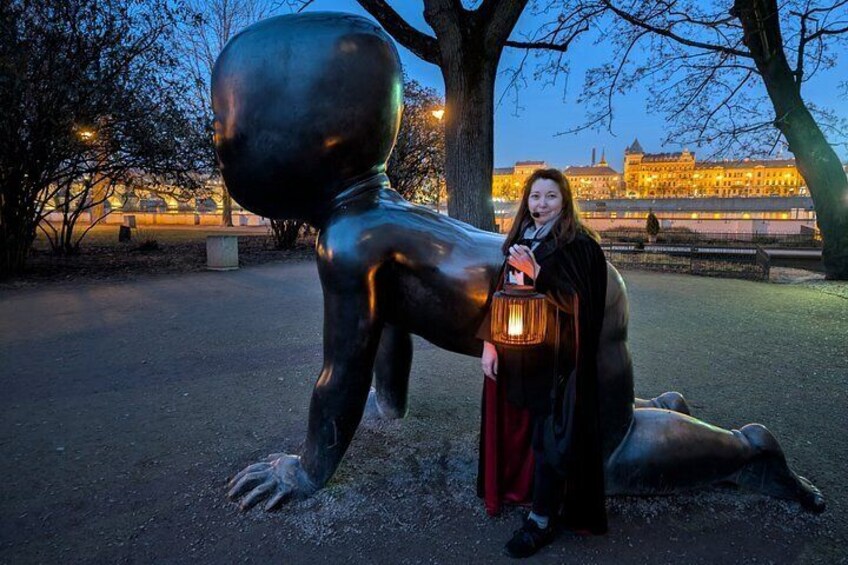 A person standing next to a large bronze statue of a human figure in a park at dusk. 3