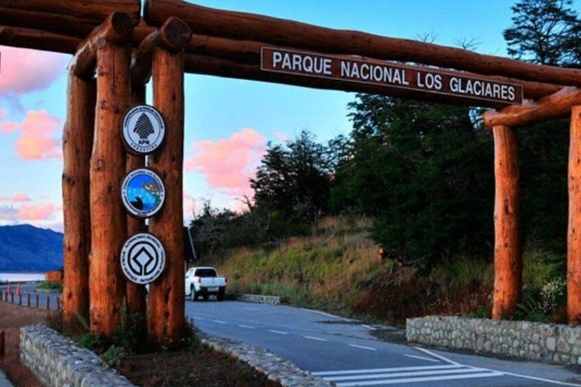 A wooden archway with a sign reading 'Parque Nacional Los Glaciares' and three circular signs with symbols. 2