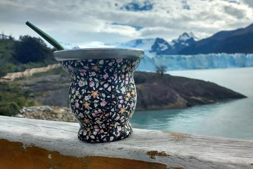 A traditional South American drinkware on a wooden ledge with a scenic view of a glacier and mountains in the background. 1