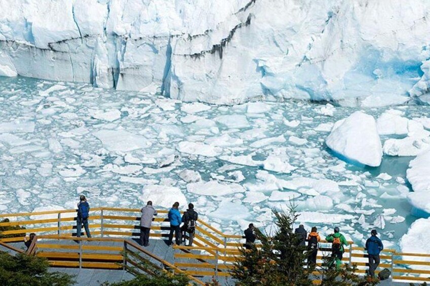 A group of people observing a glacier with icebergs in a body of water. 4