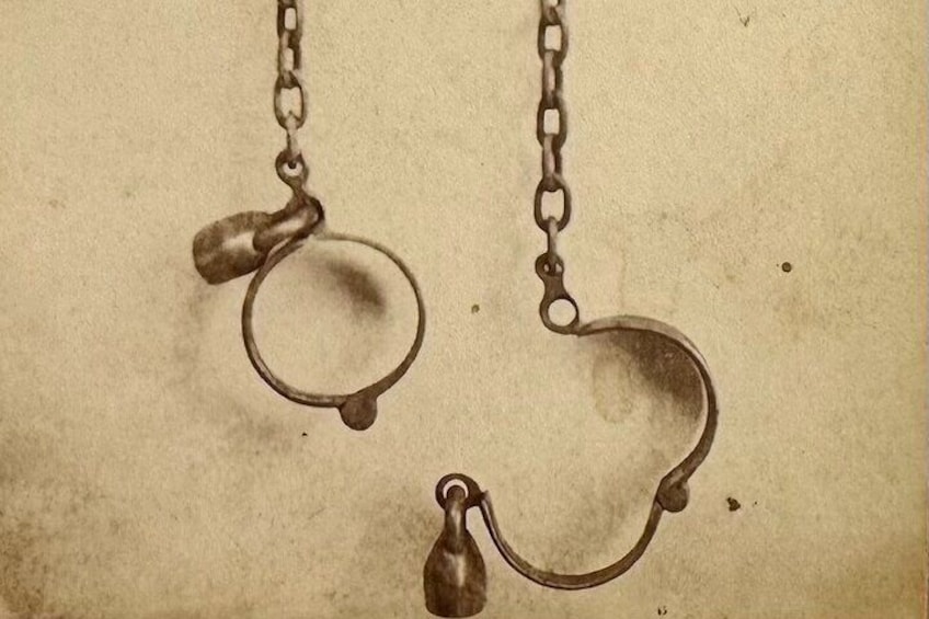 A pair of antique handcuffs hanging from a chain. 3
