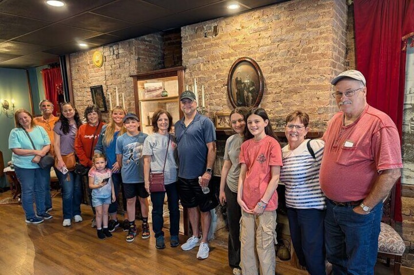 A group of people standing indoors with a brick wall and a framed picture in the background. 5