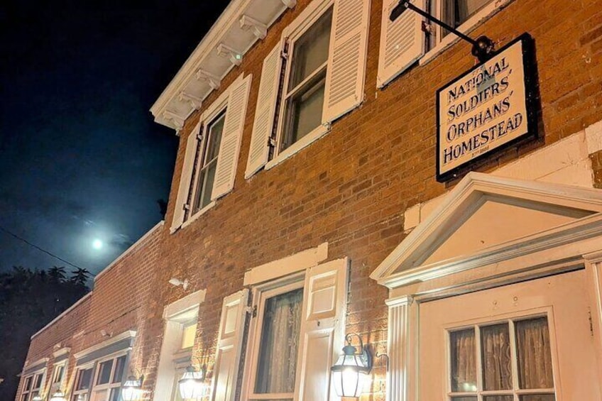 A brick building with a sign reading "National Soldiers' Orphans' Homestead" at night. 4