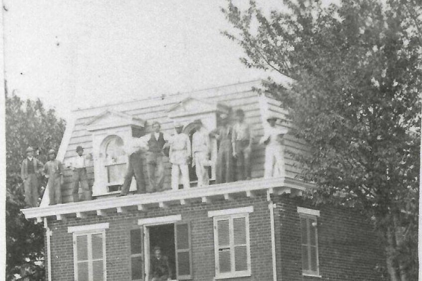 A group of people standing on a wooden structure attached to a brick building. 2