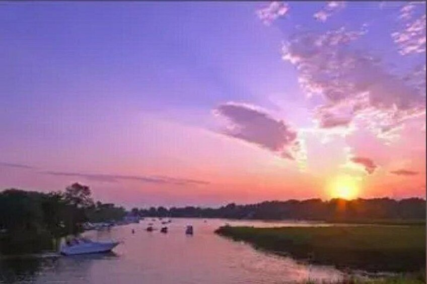 A sunset over a river with boats and a boat docked on the left. 2