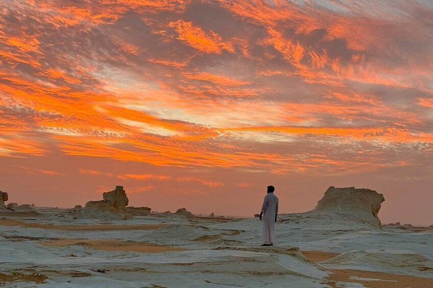 Eine Person steht in einer Wüstenlandschaft mit Felsformationen und einem Sonnenuntergangshimmel. 1
