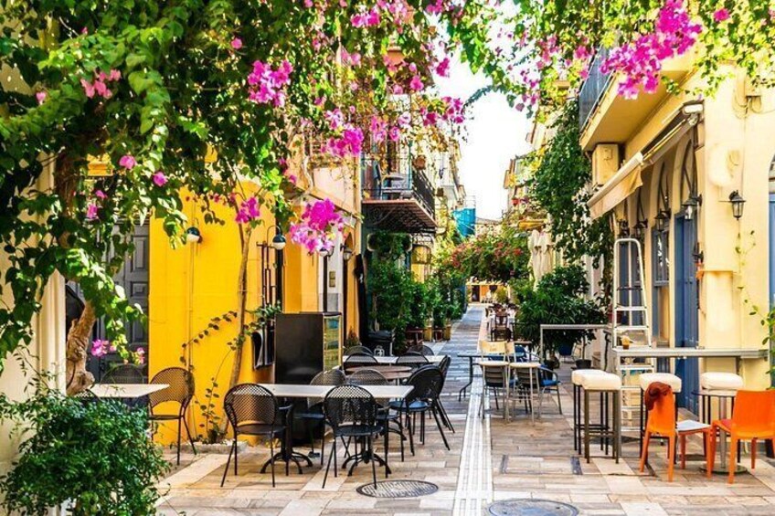 Ein Straßencafé mit Tischen und Stühlen, umgeben von gelben Gebäuden und rosa Blumen. 4