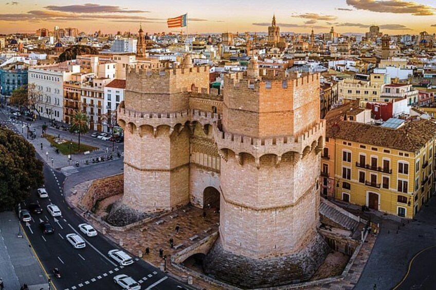 A historic tower with two prominent towers, surrounded by urban buildings and a clear sky. 5