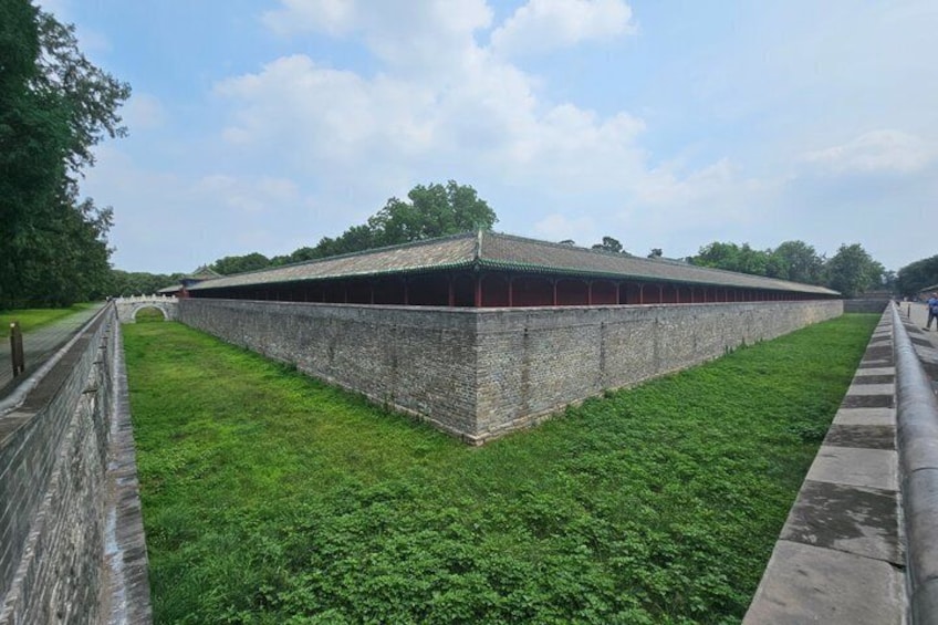 A large brick structure with a green roof, surrounded by a grassy area and a stone wall. 4