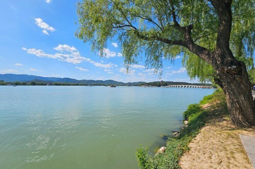 A calm lake with a tree-lined shore, a distant bridge, and mountains in the background. 3