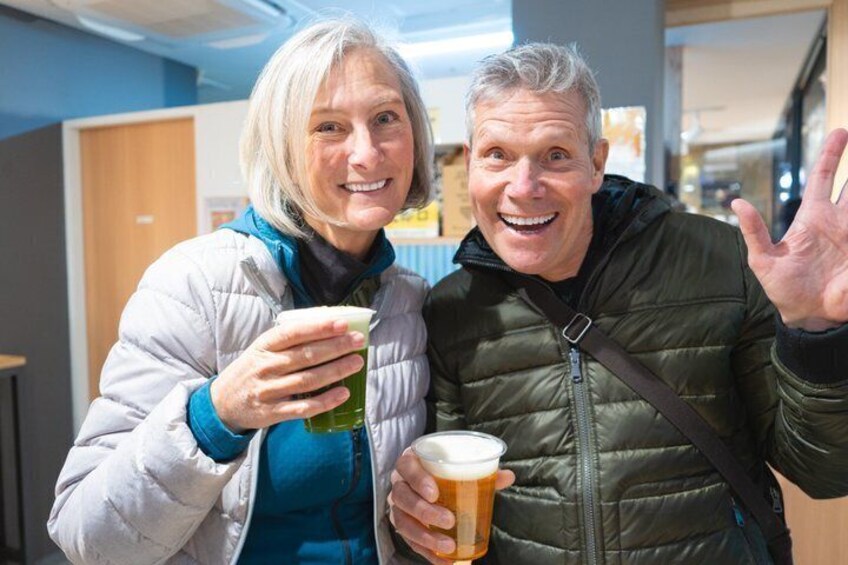 Two people holding glasses of beer in an indoor setting with a blue wall and wooden door in the background. 3