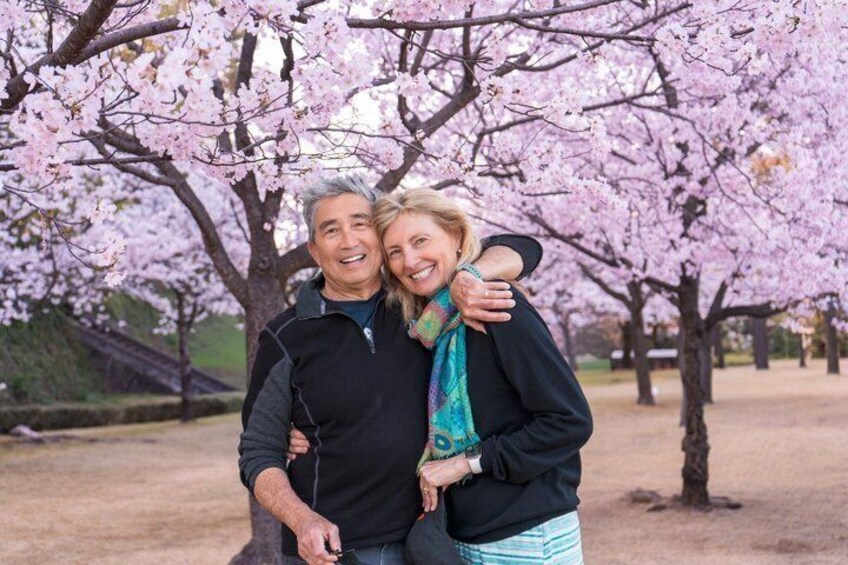 Two people embracing under cherry blossom trees in a park. 5