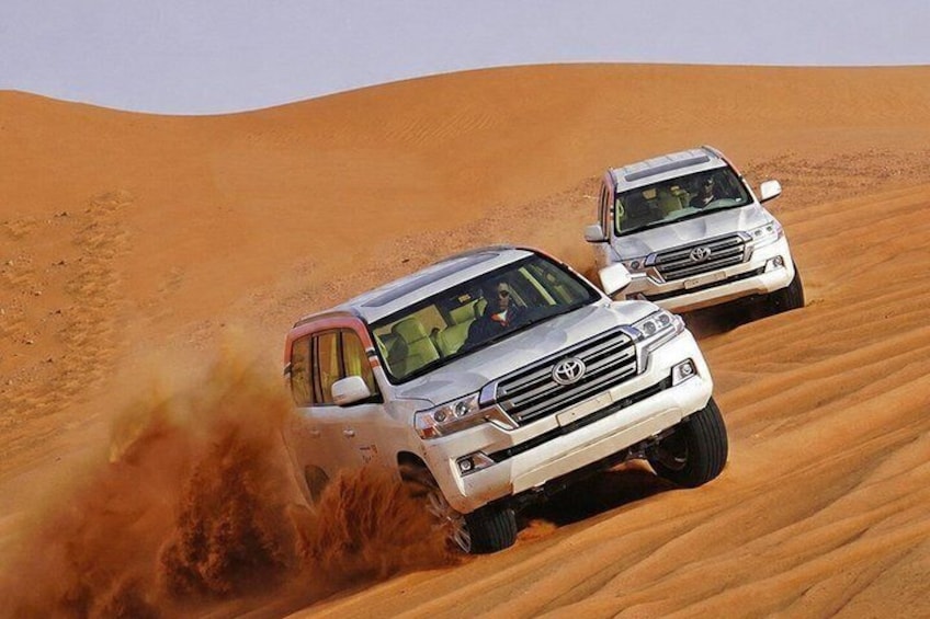 Two off-road vehicles driving through a desert with sand dunes. 2