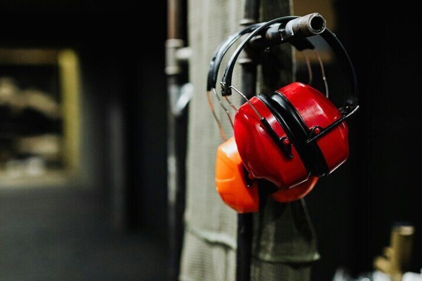 A pair of red and orange ear protection headphones hanging on a metal structure. 5