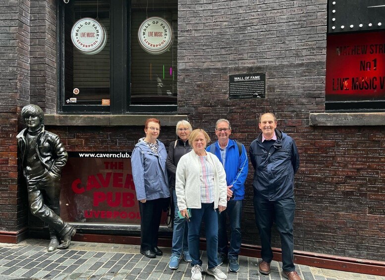 A group of people standing in front of a brick building with a sign that reads "WALL OF FAME LIVE MUSIC LIVERPOOL". 2
