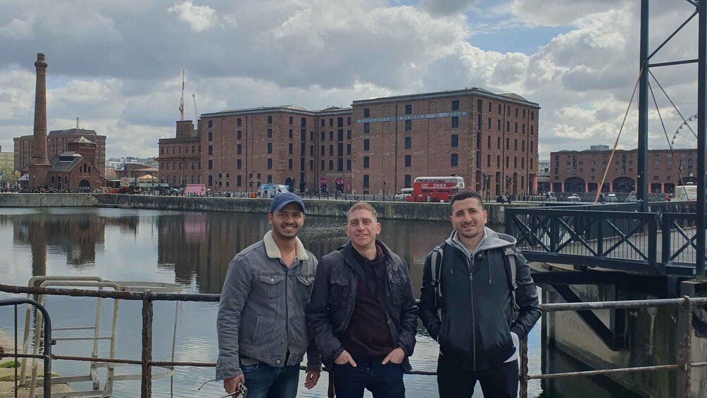 Three men standing by a waterfront with a historic building and a red double-decker bus in the background. 5