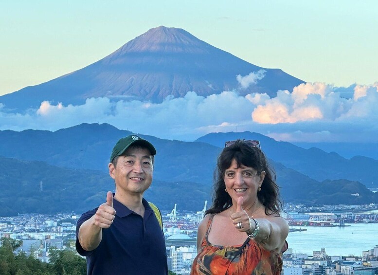 Two people giving thumbs up in front of a cityscape with a volcano in the background. 4