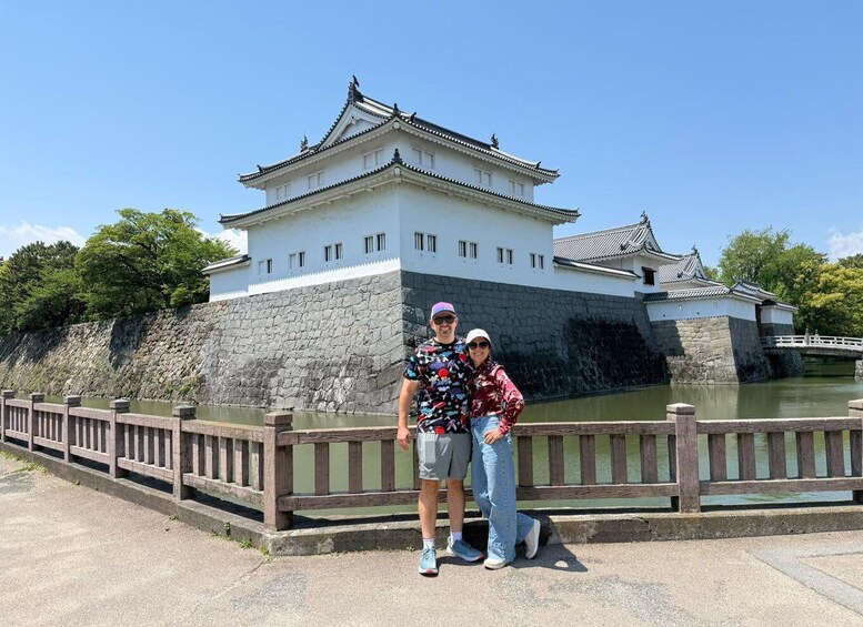 A couple standing in front of a traditional Japanese castle with a stone wall and a wooden fence. 5