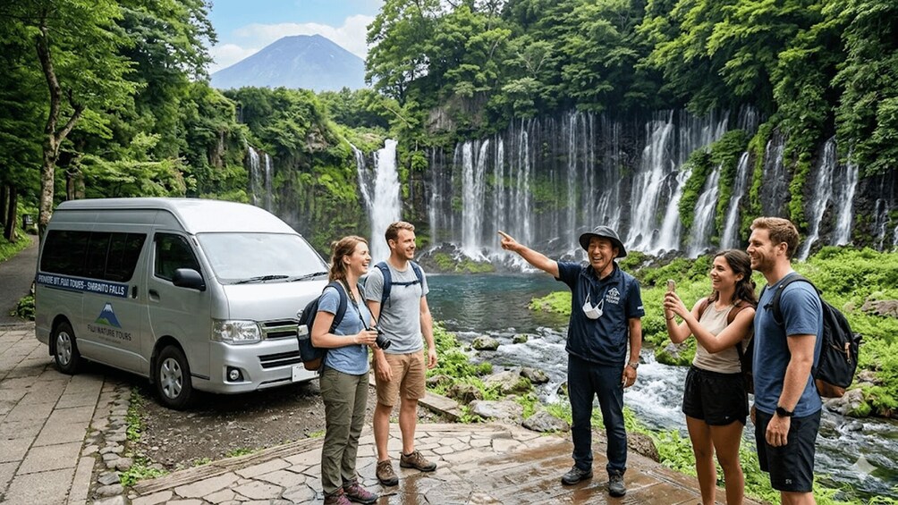 A group of people standing by a waterfall with a van labeled 'Fiji Nature Tours' parked nearby. 2