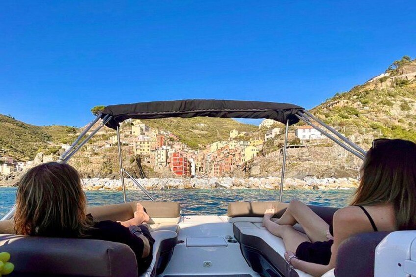 A boat with two passengers, a rocky coastline, and colorful buildings in the background. 3