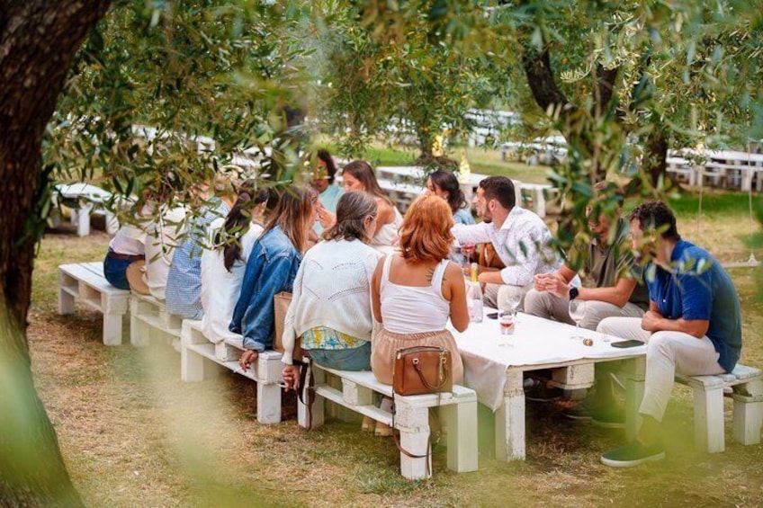 People seated at tables outdoors under trees. 1