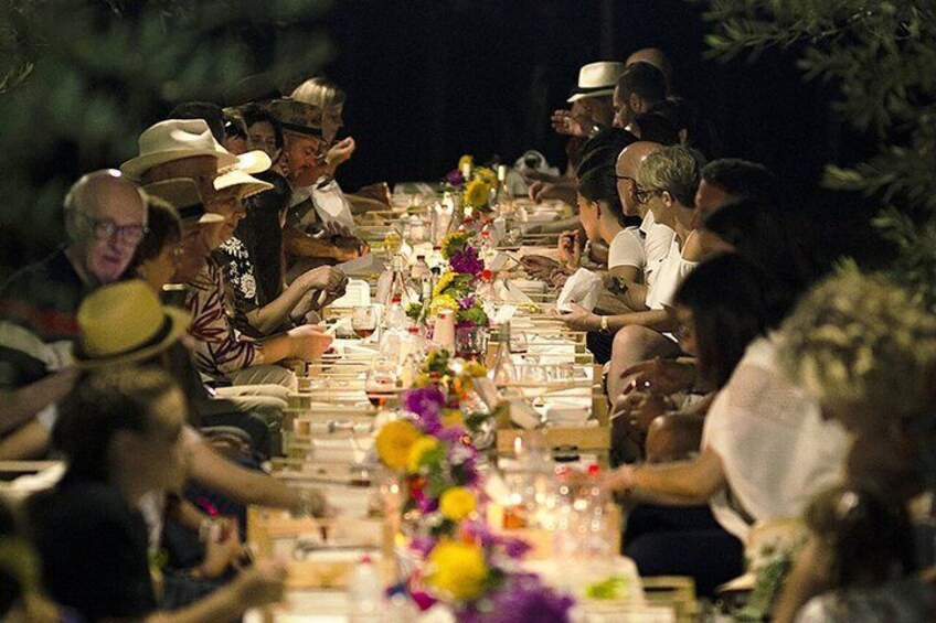 A group of people seated at a long table outdoors at night, decorated with flowers and candles. 4