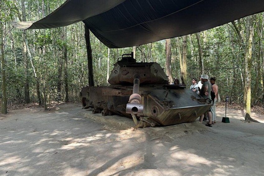 A military tank displayed outdoors under a canopy in a forested area. 4