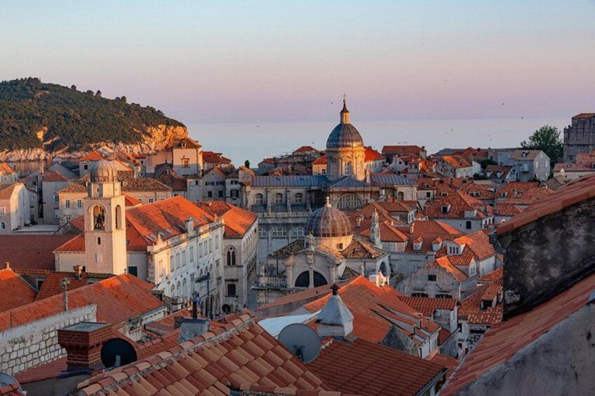 A coastal cityscape with historic buildings, a prominent dome, and a hill in the background. 1